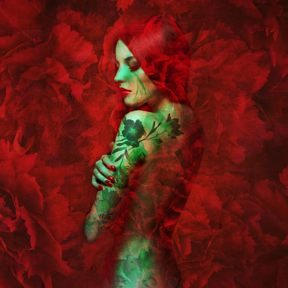 A woman with body tattoos poses gracefully among vibrant red flowers.